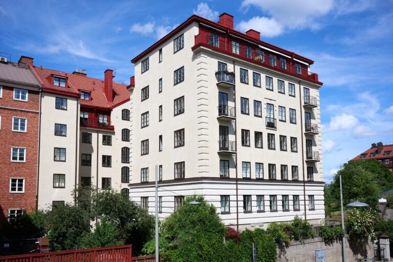Ljust putsat flerbostadshus med balkonger och rött plåttak