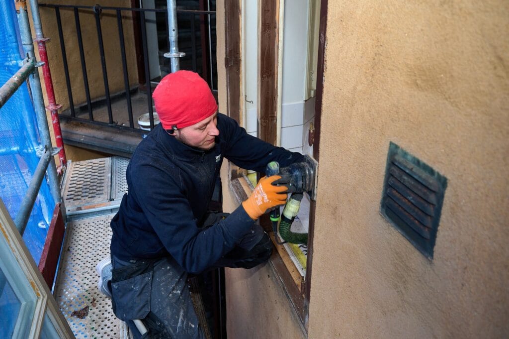 Hantverkare slipar fönsterkarm från ställningen vid fönsterrenovering