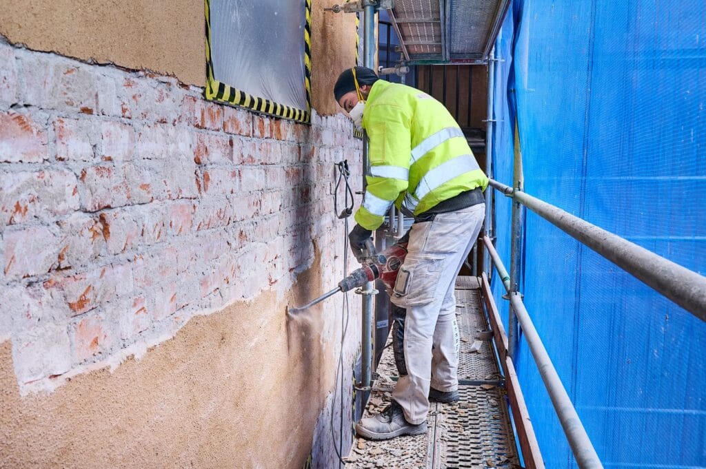 Hantverkare lagar tegelfasad från ställning under fasadrenovering