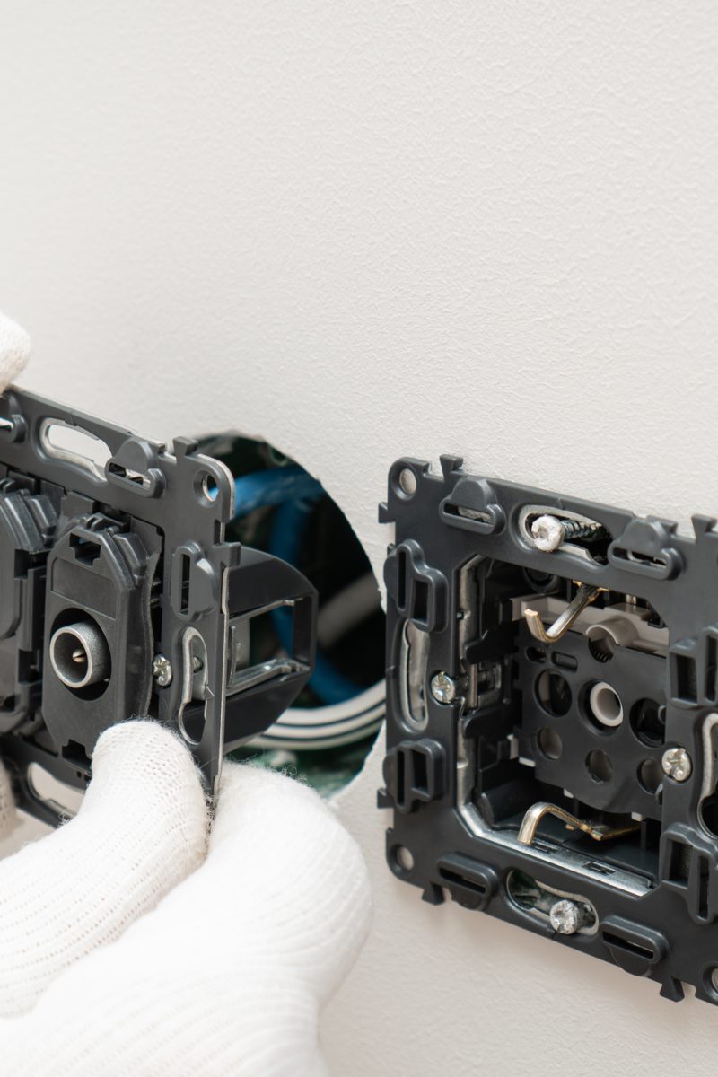 An electrician is installing multifunction outlet with internet connection, tv and electric socket , wires while home renovating.