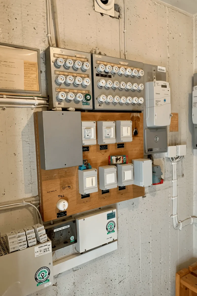 Äldre elcentral med porslinssäkringar, gruppcentraler och elmätare i fastighetens elrum