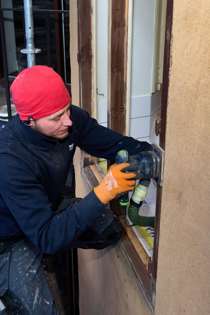 Hantverkare slipar fönsterkarm från ställningen vid fönsterrenovering